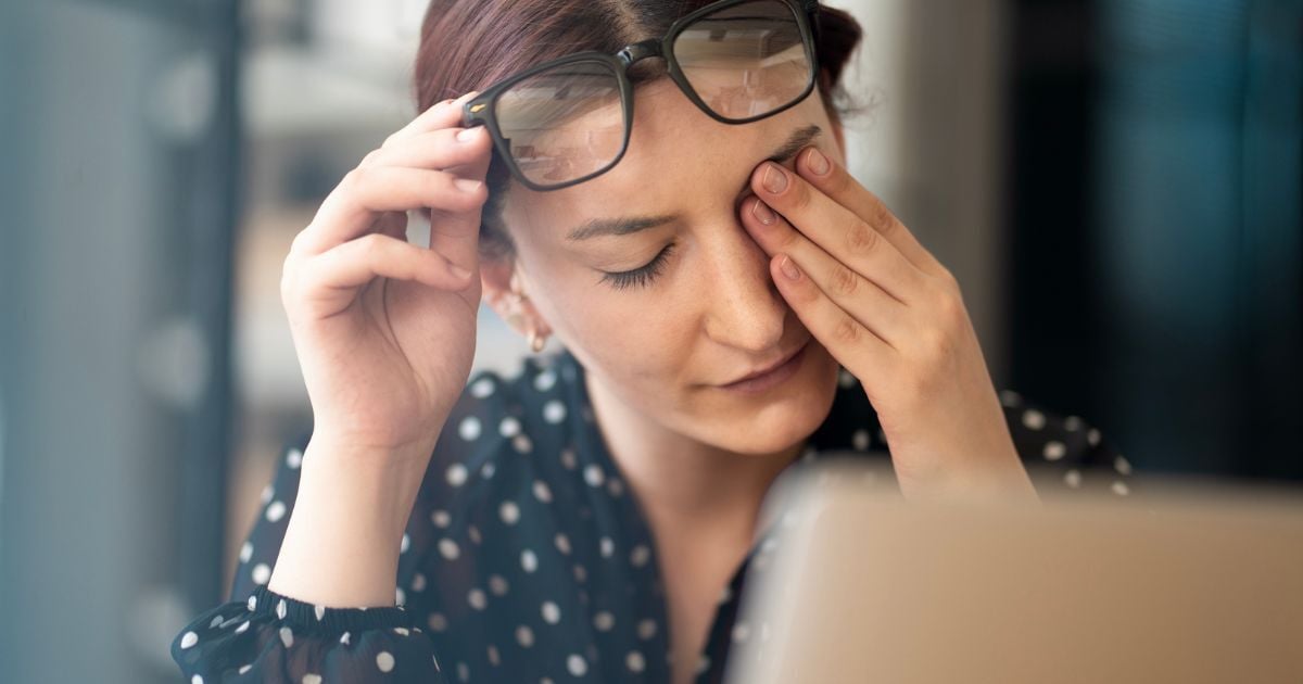 A woman rubbing her stinging eyes caused by chronic dry eye.
