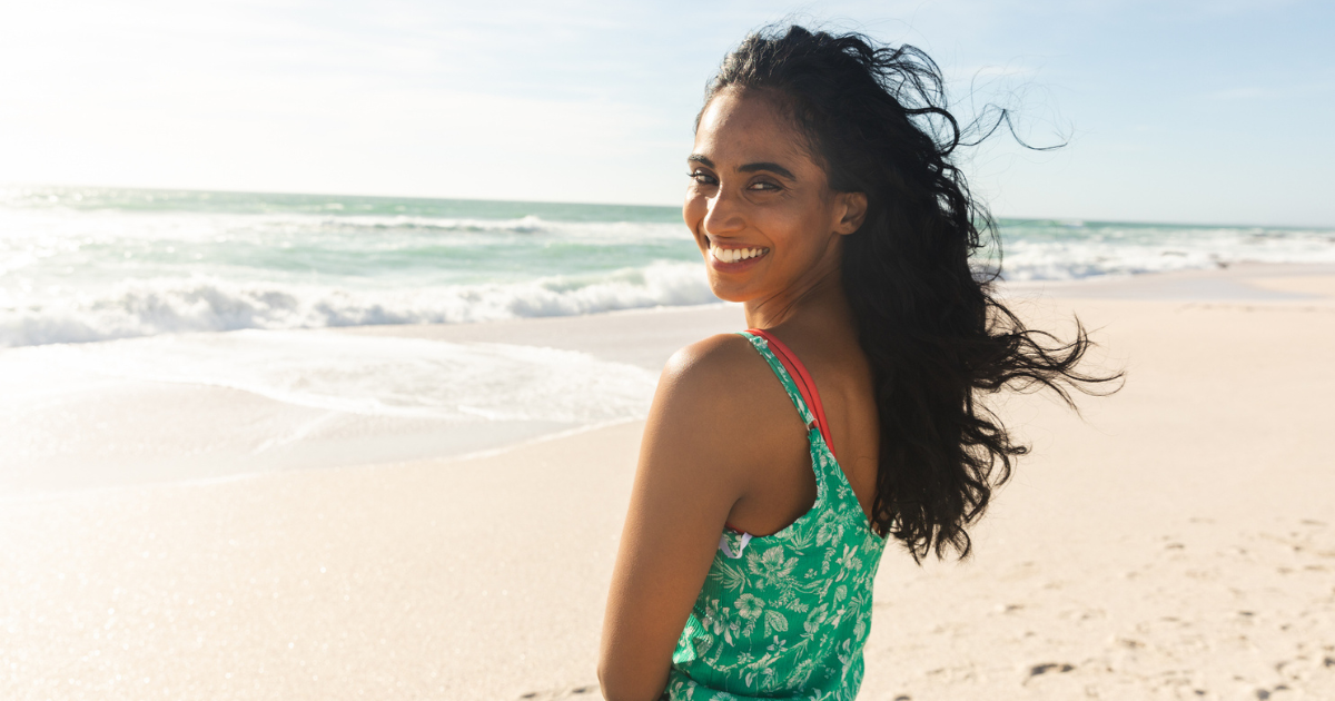 A woman at the beach smiling because her eye allergies aren't bothering her.