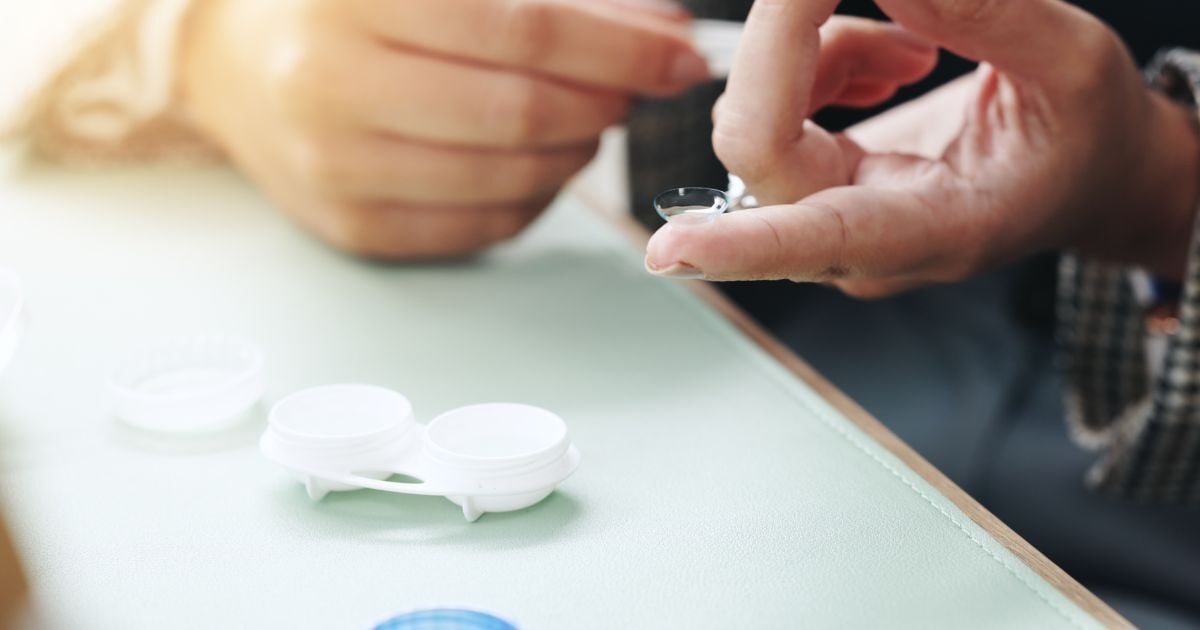 A person with a contact lense on their finger next to a contact lense case.