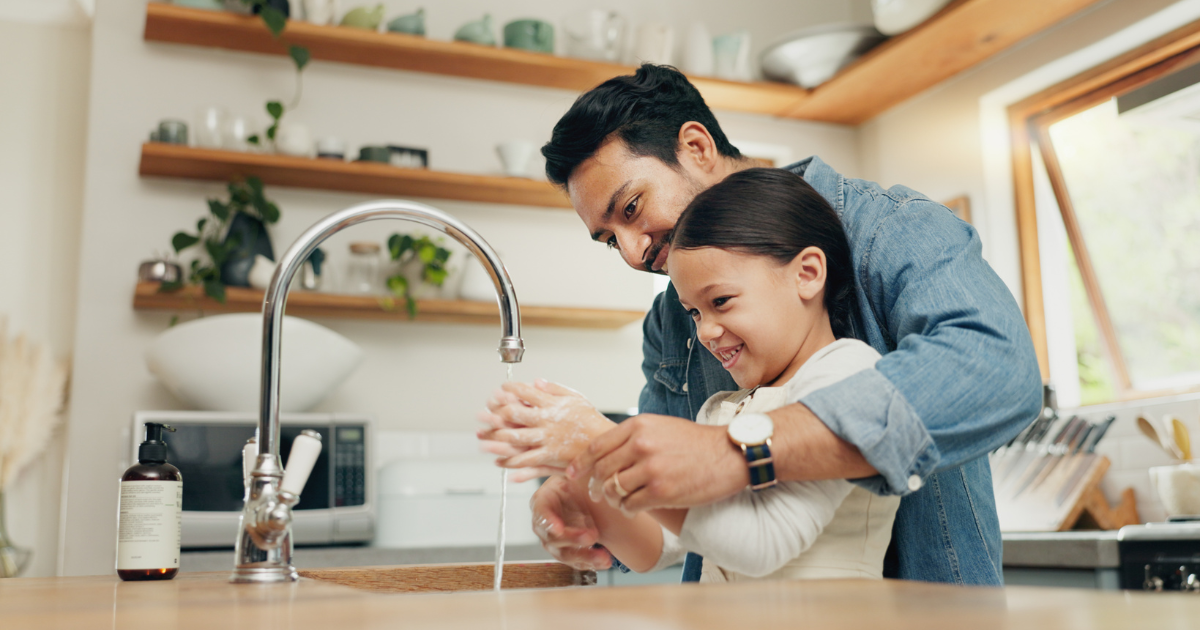 A yound girl washing her hands with her dad.