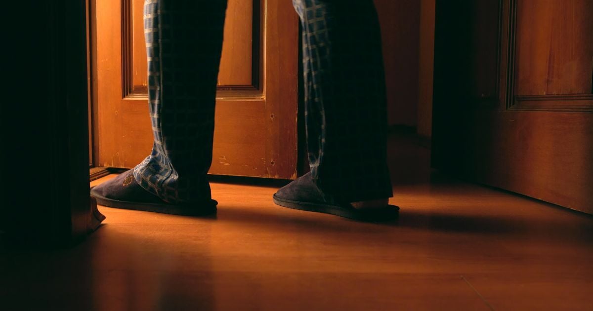 An older man walking to the bathroom at night in a dark hallway.