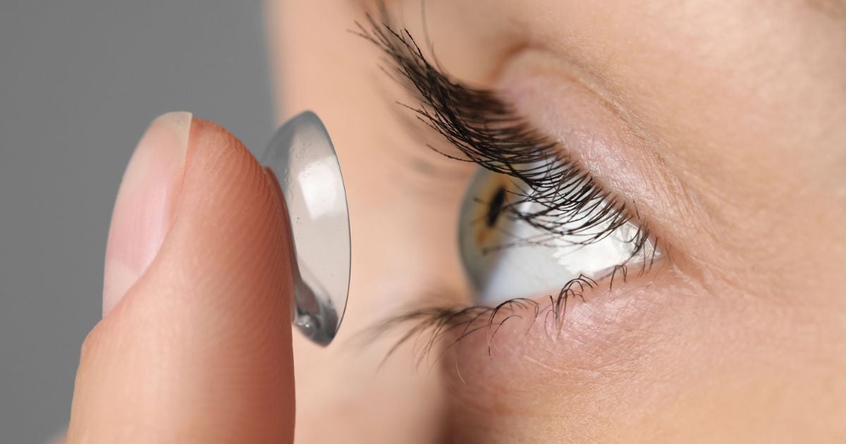 A woman is putting a contact lens in her eye.