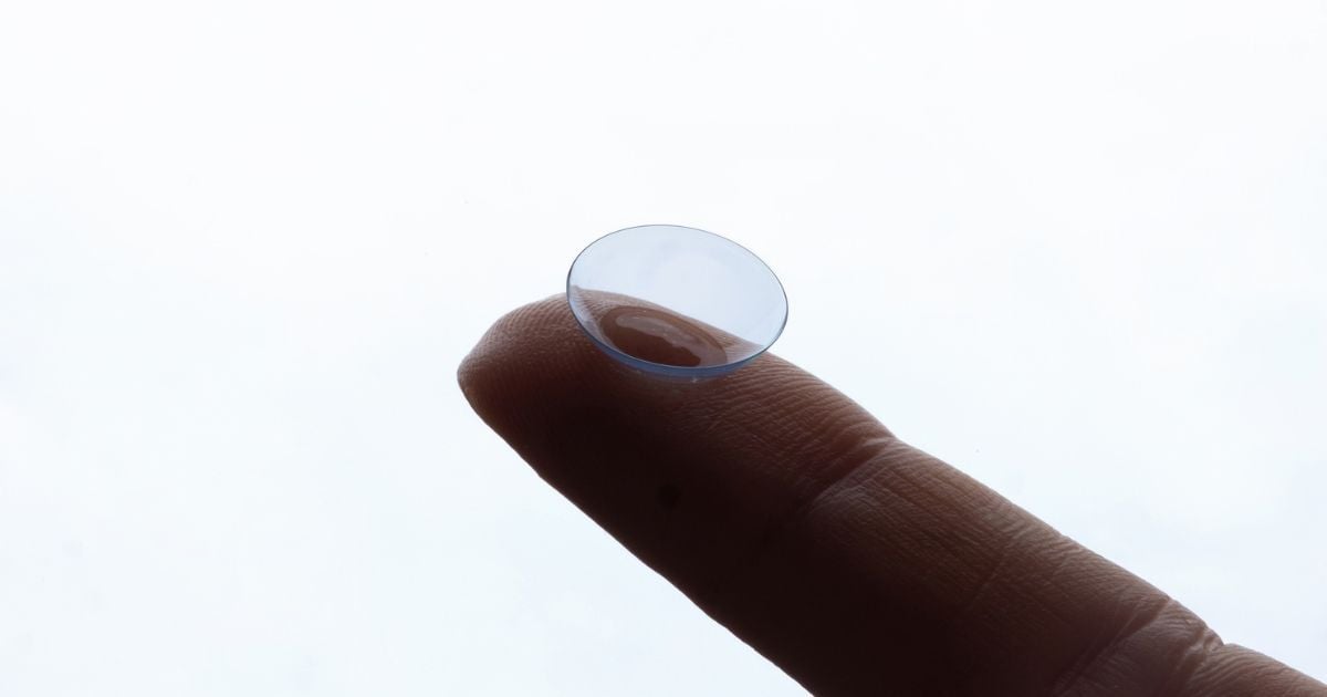 A close up of a finger holding a contact lense at the tip.