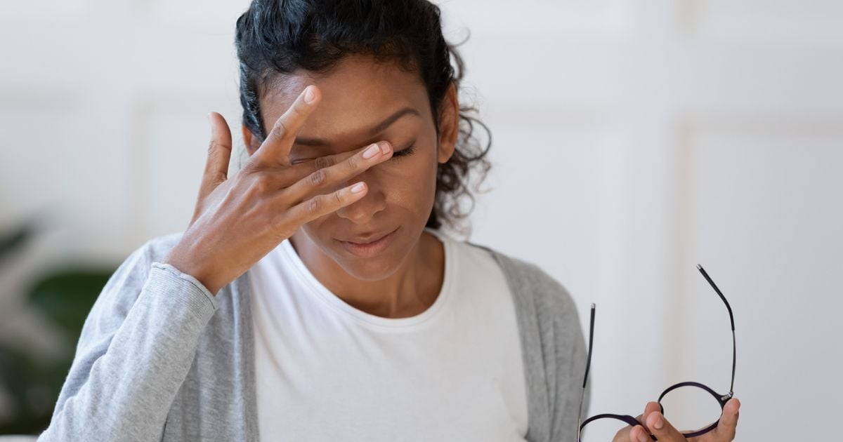 A woman with dry eye takes off her glasses to rubs her irritated eyes