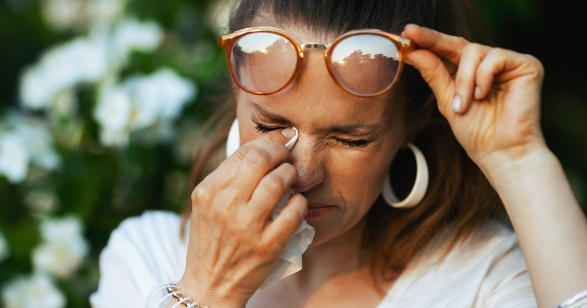 A woman outside blotting her eyes that are tearing and itchy from allergies.