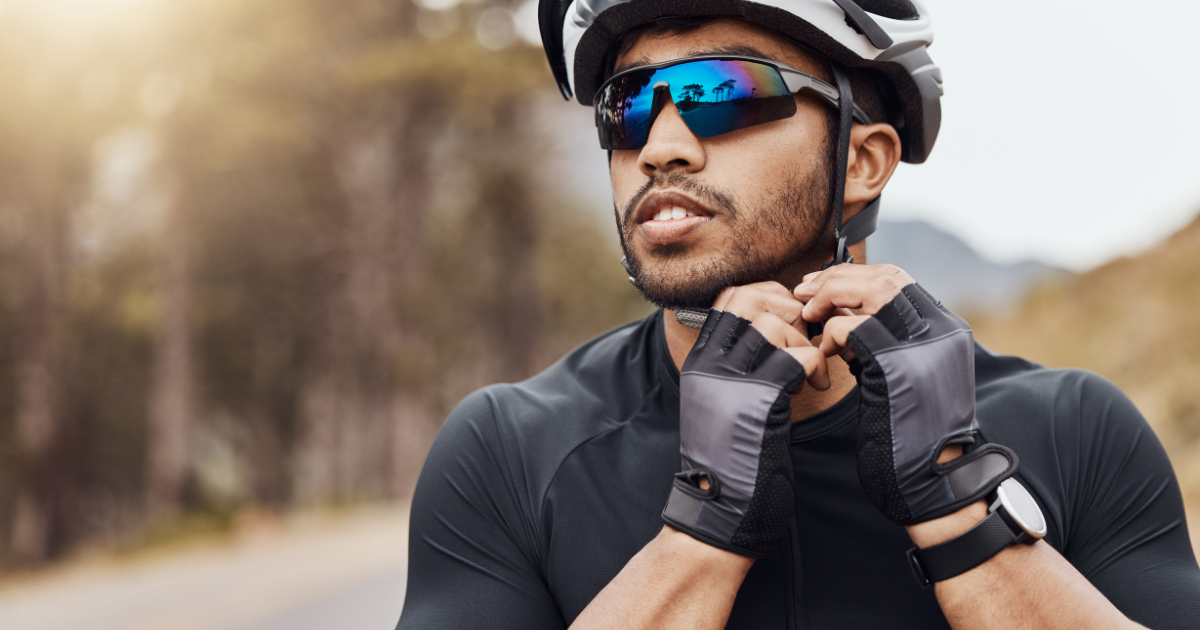 A man putting on his bike helmet wearing wrap around sunglasses.