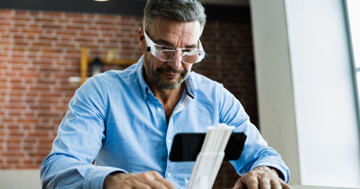 An older man using low vision aids to read his phone.