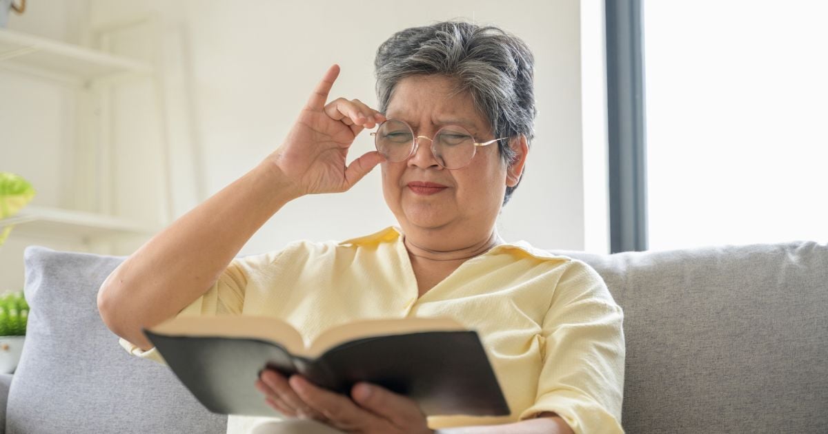 A older woman squinting at a book having a hard time seeing even with glasses.