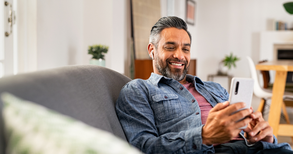 A man on his couch looking at his phone after having light adjustable lens surgery.