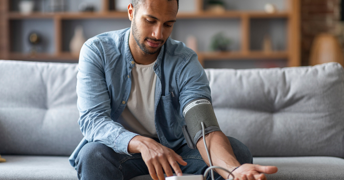 A man sitting on his couch taking his blood pressure.