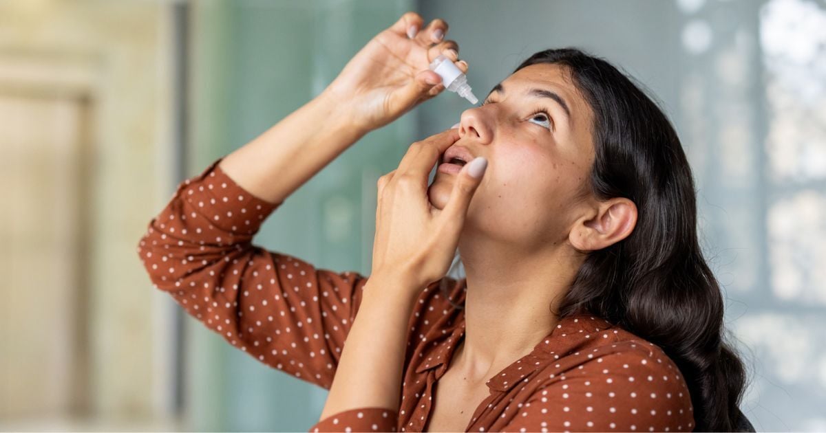 A woman places eye drops in her eyes to treat her meibomian gland dysfunction.