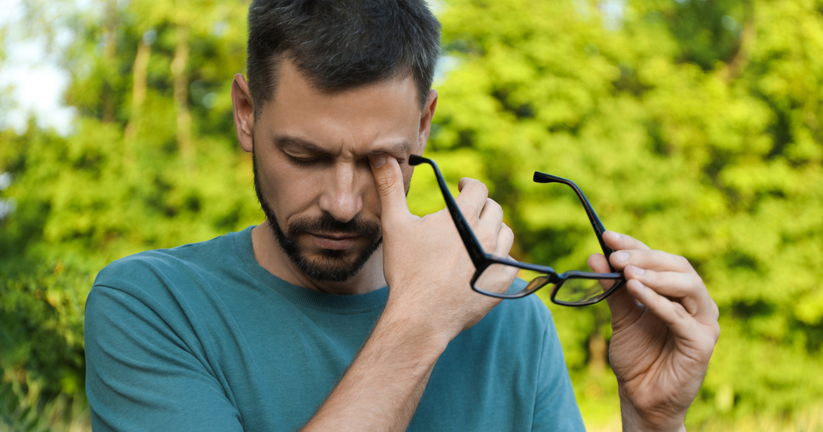 A man taking his glasses off to rub his allergy eyes.