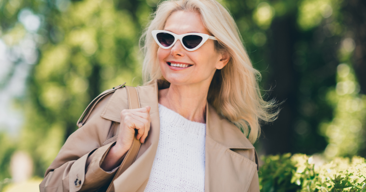 An older woman wearing white sunglasses smiling on her walk.