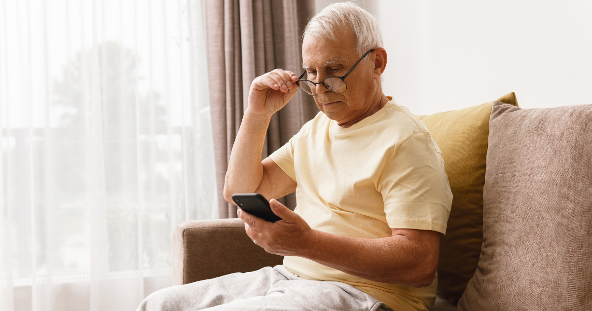 An older man with glasses reading his phone.