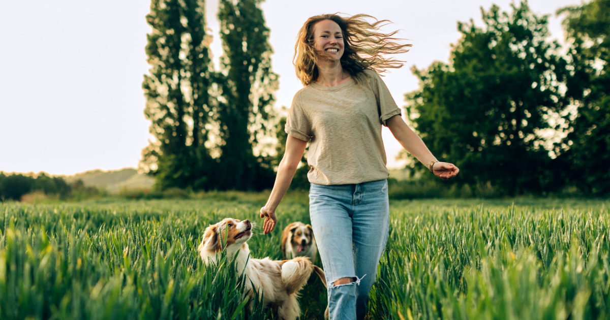 Happy woman walking through a field with her dogs after getting LALs.