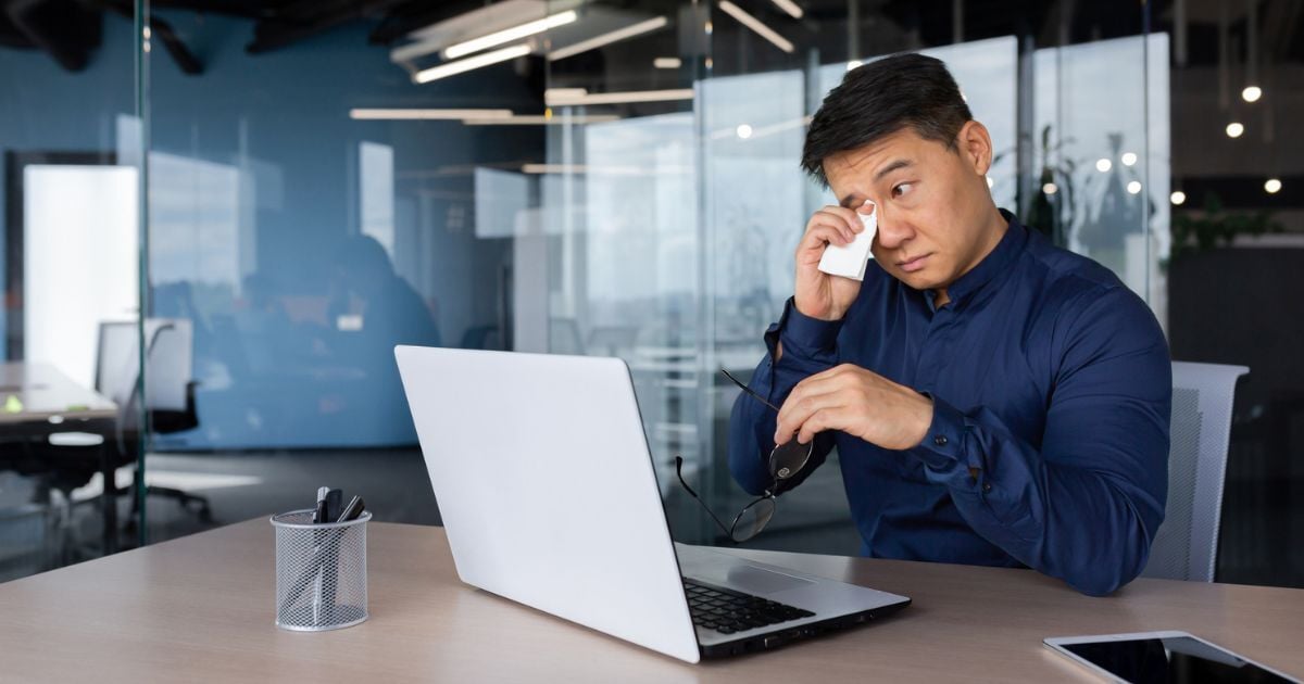 A man dabs the corner of his eye with a tissue.