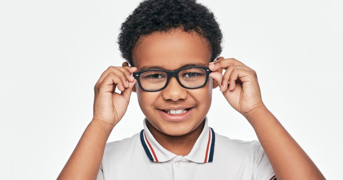 A young boy in a white shirt adjusts his glasses.