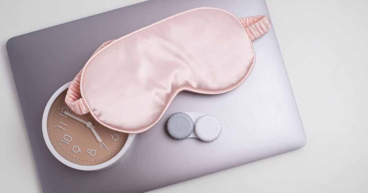 An eye mask, clock, and contact lense case on a pillow.