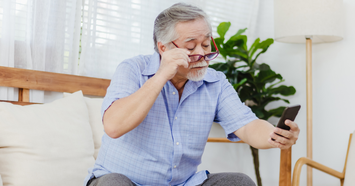 An older man trying to read his phone but struggling because of presbyopia.